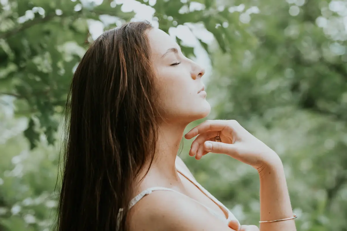 Mujer con los ojos cerrados respirando tranquila entre árboles